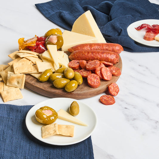Platter of assorted meats, cheeses, and olives on a wooden board with crackers.