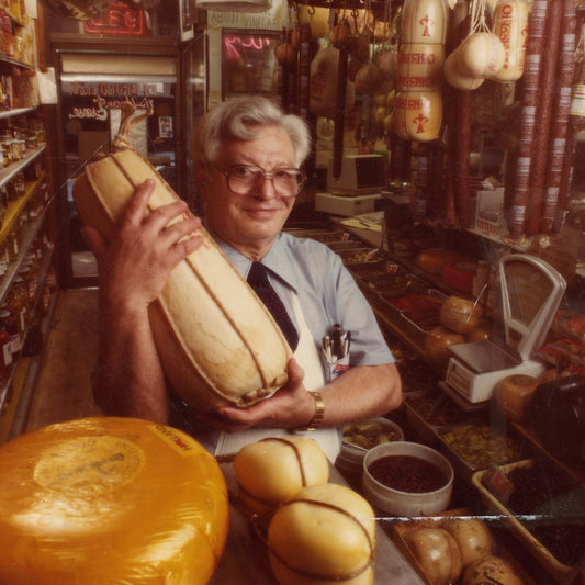 Danny holding a large piece of cheese in a deli or market setting