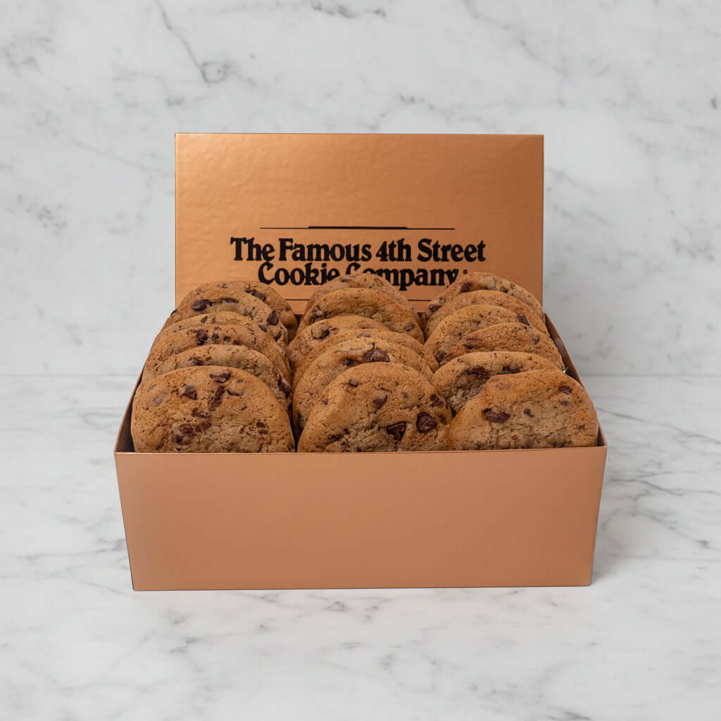 A box of chocolate chip cookies from The Famous 4th Street Cookie Company, shown in a metallic rose-gold colored box with the brand name printed on the inside lid, set against a white marble background.