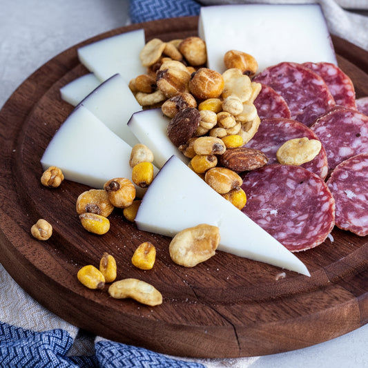 Wooden platter with sliced salami, cheese, and nuts on a light background