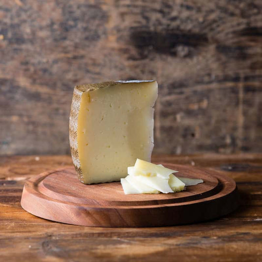 A wedge of Manchego cheese on a wooden cutting board with a few pieces cut off and placed beside it.