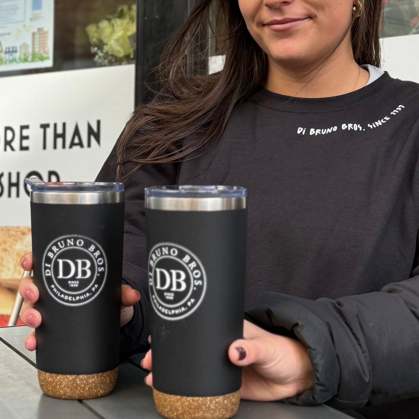 Julia holding two black tumblers with cork bases, featuring the DB logo, in an outdoor setting.