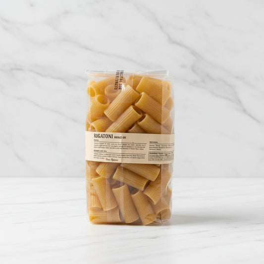 Bag of pasta with a label on a white surface, with a cardboard box in the background.