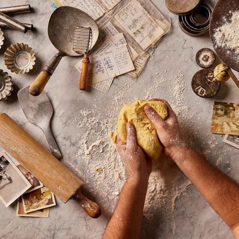 Hands kneading dough on a rustic kitchen counter with various baking tools and ingredients.