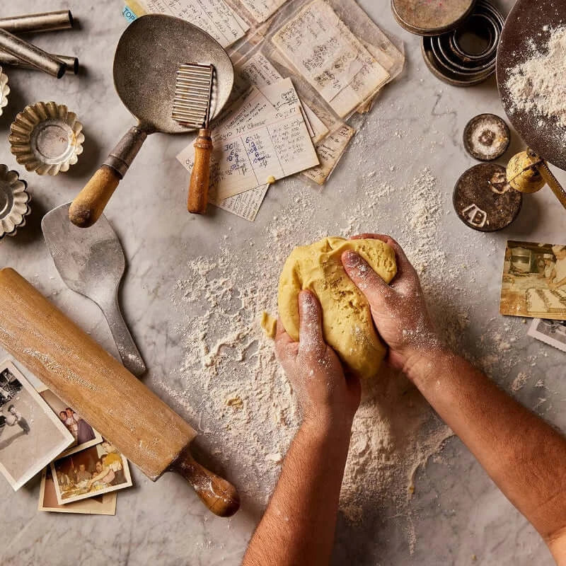Hands kneading dough on a rustic kitchen counter with various baking tools and ingredients.