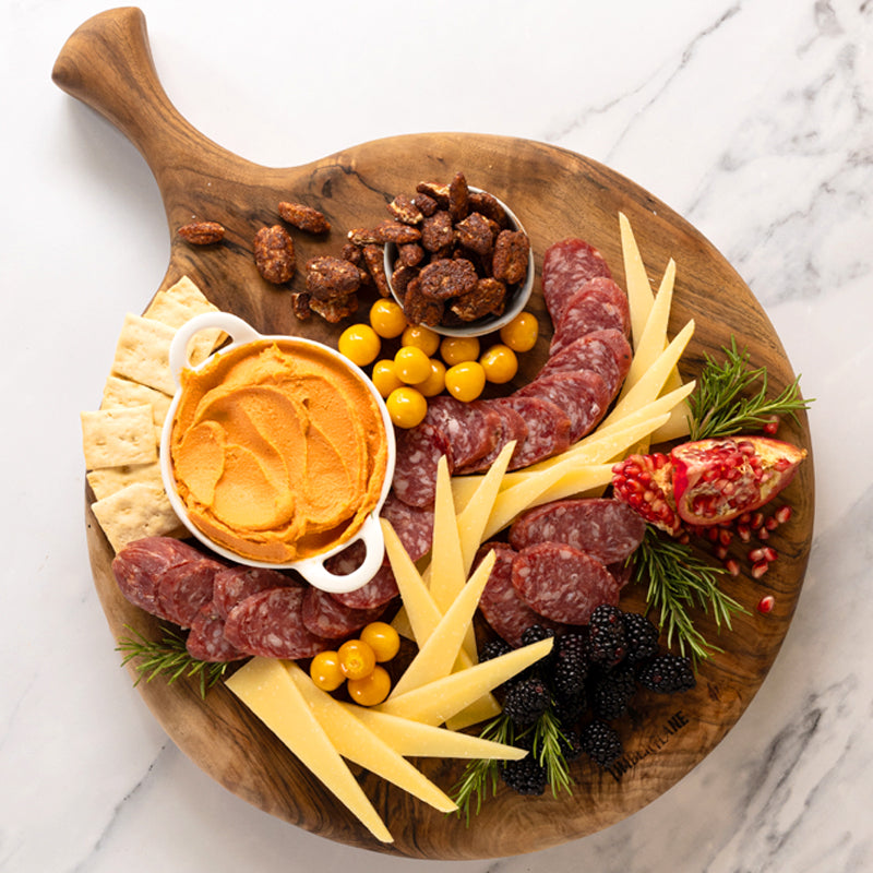 A gourmet gift box from Di Bruno Bros featuring a selection of cheeses, meats, and crackers arranged on a wooden board. Includes cheese slices, salami, crostini, and candied nuts.