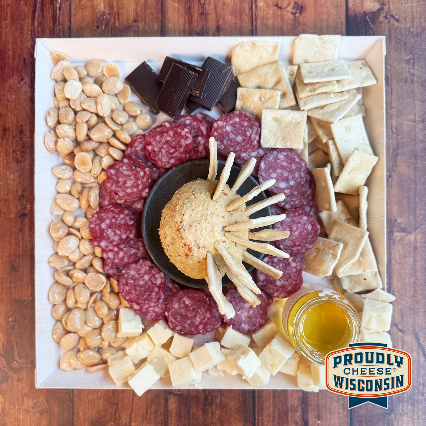 An array of gourmet cheese, meats, and crackers neatly arranged on a cheese board, with a small bowl of honey and almonds, salami.