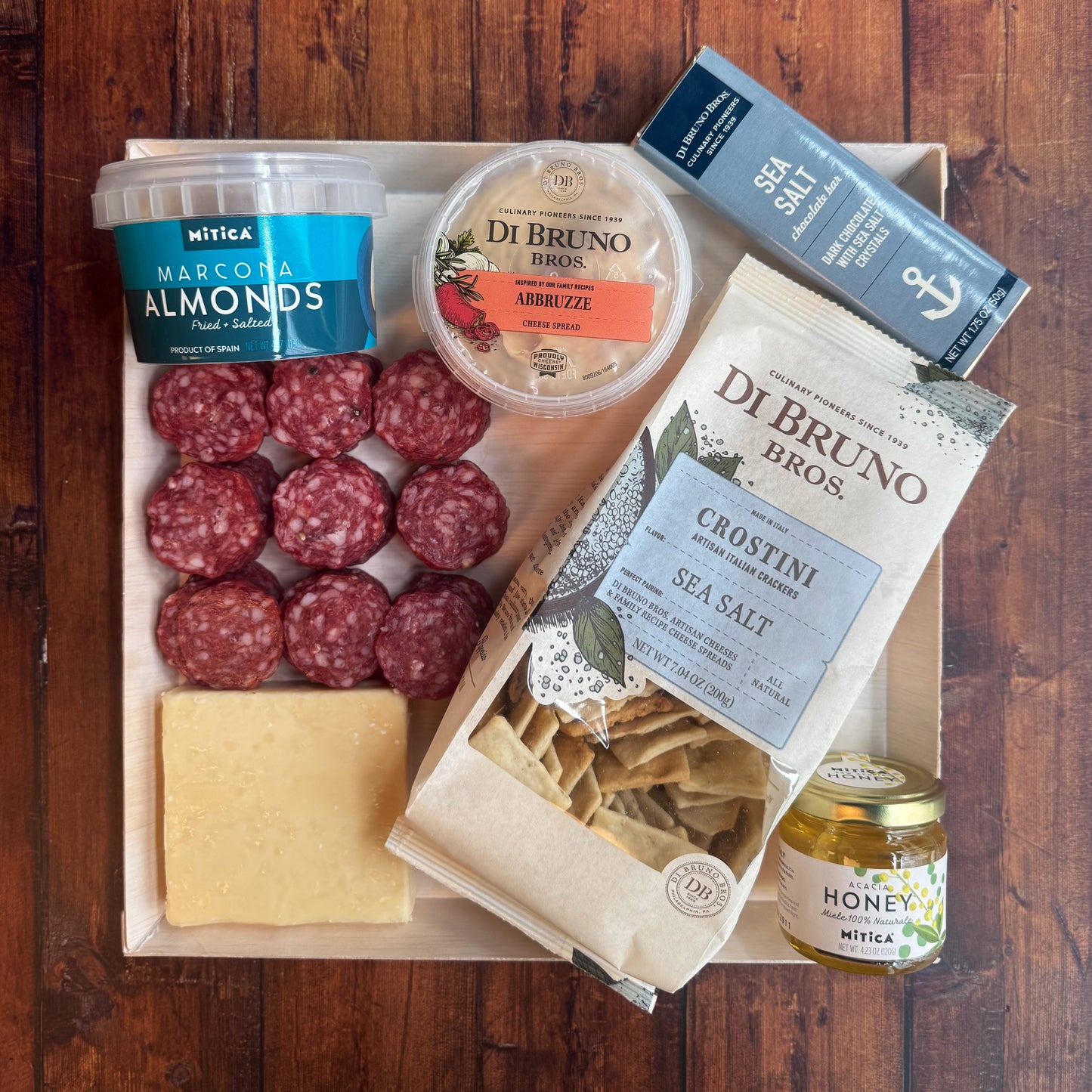 An array of gourmet cheese, meats, crackers, small jar of honey, almonds, and salami neatly packaged on a board.