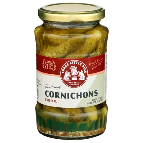 A jar of Three Little Pigs Traditional Cornichons in vinegar, with a label showing the brand logo and the product name.