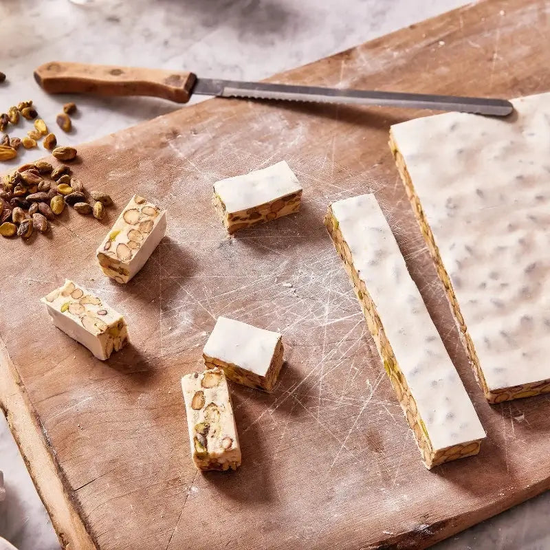 Nougat pieces on a wooden board with nuts and a knife