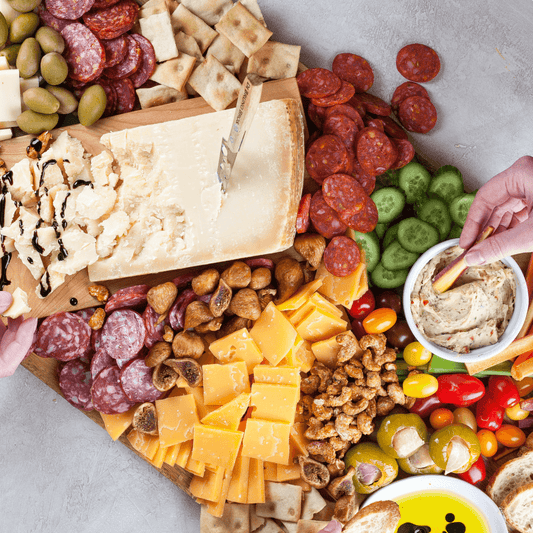 Platter of assorted cheeses, meats, and vegetables with a hand reaching for a cracker.