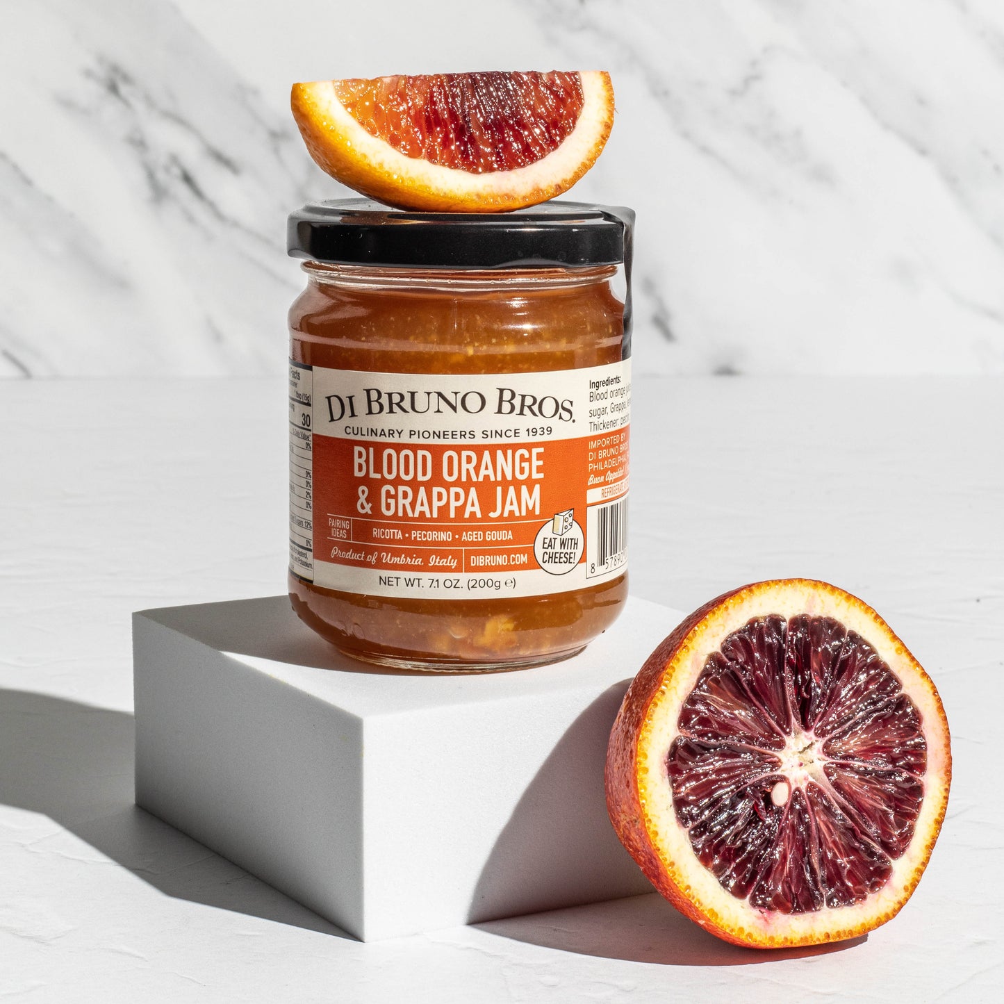 Jar of Di Bruno Bros. Blood Orange & Grappa Jam with blood oranges on a marble background