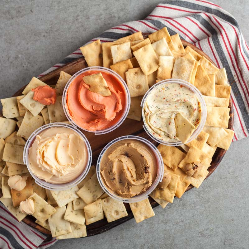 Di Bruno Bros. crostini crackers on a wooden board with four classic cheese spreads in the middle.