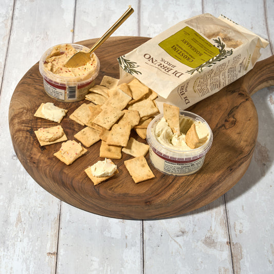 Di Bruno Bros. Crostini Sampler Set is an assortment of flavors including olive oil, parmesan, rosemary, and sea salt, displayed in front of a white background with scattered crostini crackers.