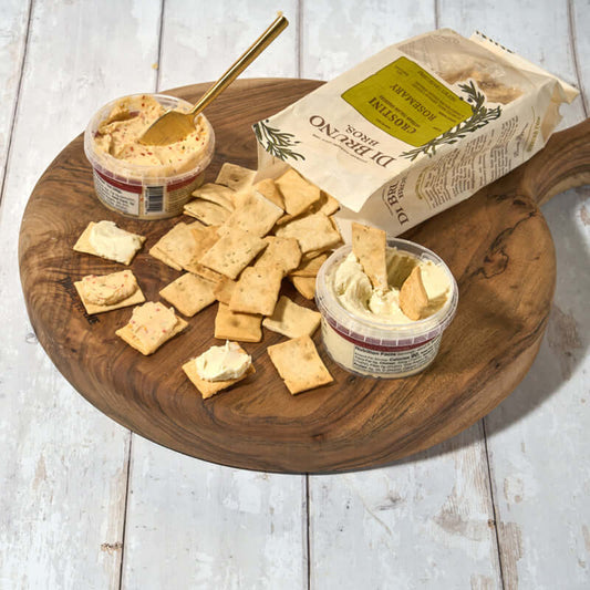 Di Bruno Bros. Crostini Sampler Set is an assortment of flavors including olive oil, parmesan, rosemary, and sea salt, displayed in front of a white background with scattered crostini crackers.