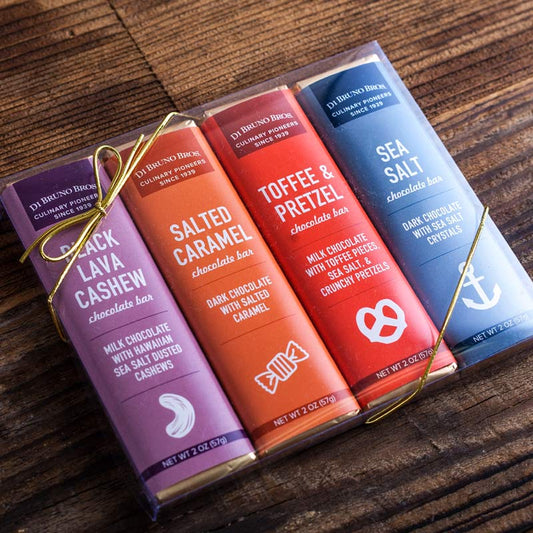 A set of four flavorful chocolate bars arranged side by side tied with decorative ribbons and labels showing Salted Caramel, Black Lava Cashew, Toffee Pretzel, and Sea Salt.