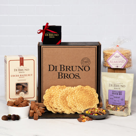 An assortment of gourmet food items from Di Bruno Bros. including chocolate truffles, cocoa biscotti, a snack mix, and pizzelles neatly packed in a gift box.