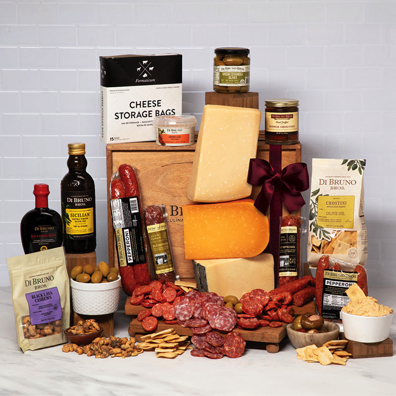 A massive assortment of Di Bruno Bros. gourmet food items including various cheeses, meats, crackers, olives, and condiments arranged on a table, presented as a gift basket.