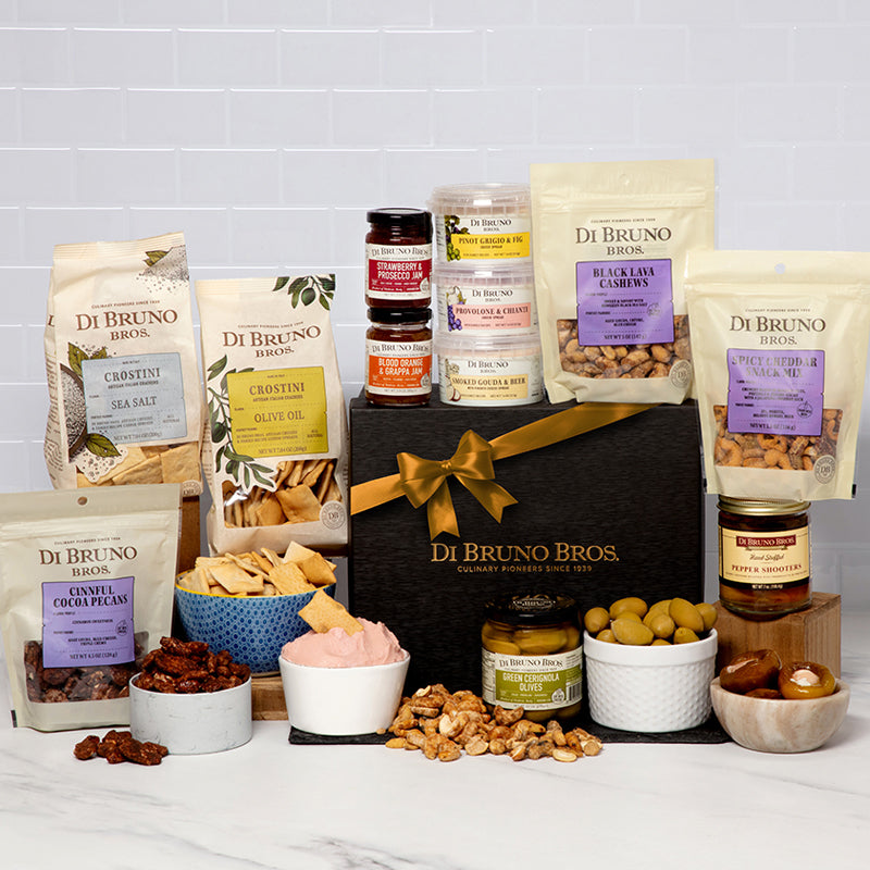 An assortment of gourmet food items including cheese spreads, crackers, olives, snack mixes, and nuts, packaged in a Di Bruno Bros. black gift box with a gold ribbon.