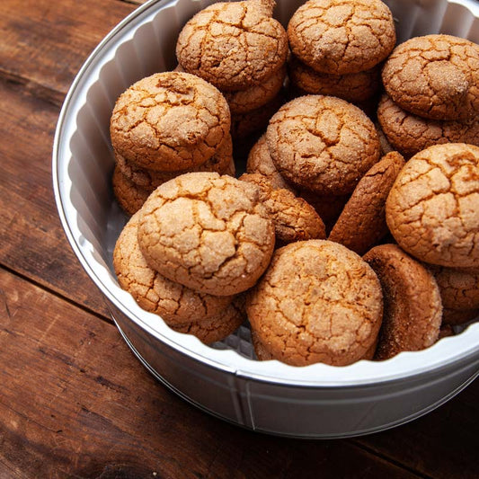 A tin of almond macaroon cookies on a wooden surface.