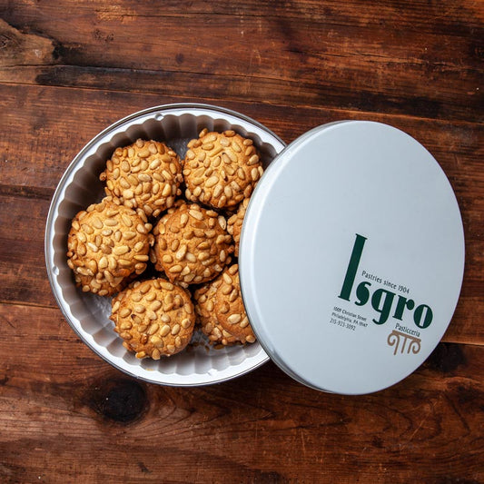 A tin of golden sugar cookies topped with pine nuts, branded with the name 'Isgro' on the lid.