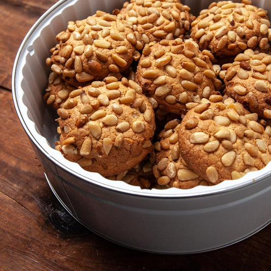 A tin of golden sugar cookies topped with pine nuts, branded with the name 'Isgro' on the lid.