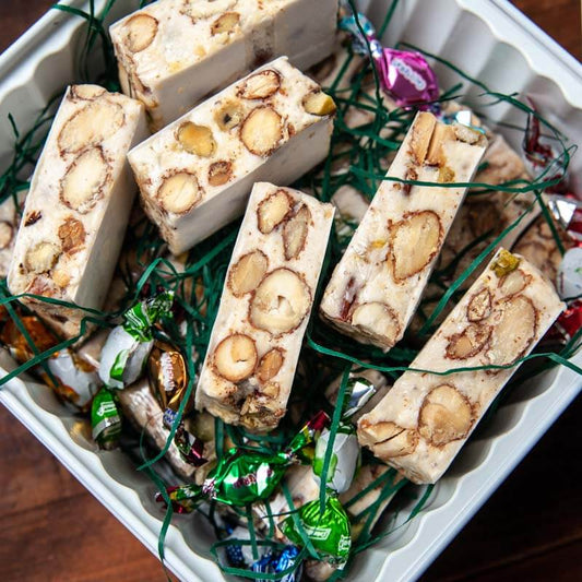 A tin of Isgro brand torrone, which is a type of nougat candy with nuts, presented in a square tin.