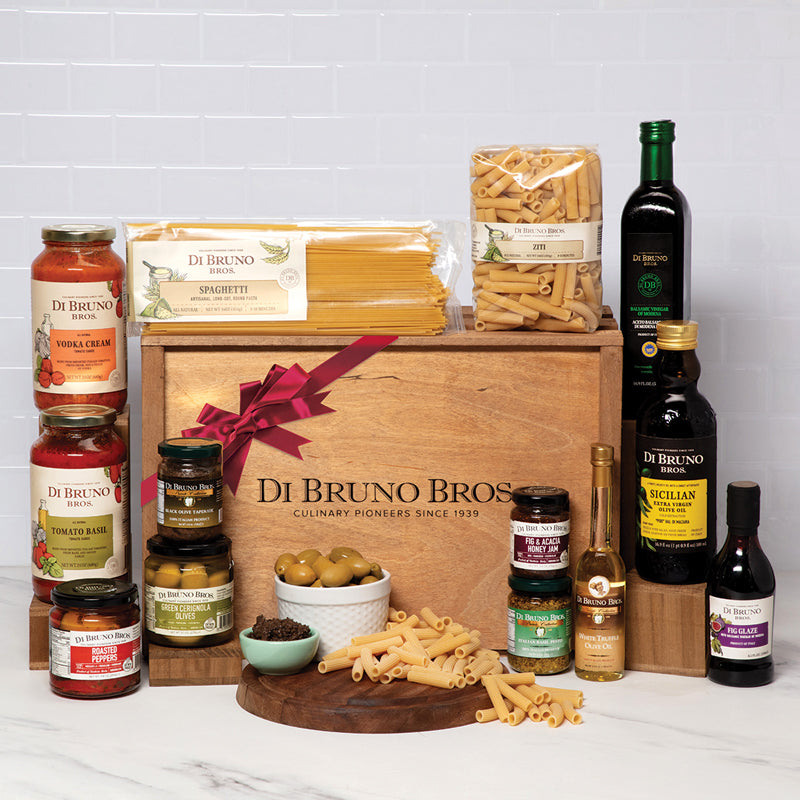 A gourmet gift crate from Di Bruno Bros. featuring an assortment of pasta, sauces, olive oils, antipasti, and other food items, presented in a wooden crate with a red bow.