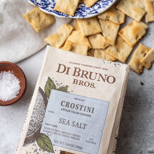 Di Bruno Bros. Crostini Sea Salt crackers packaging with crackers and a bowl of salt on a surface.