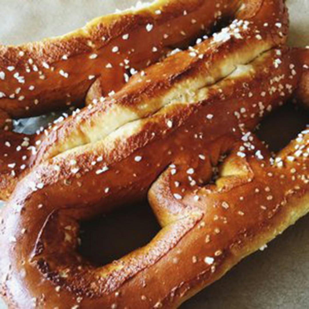 A photo of two soft pretzels with salt sprinkled on top, on a piece of parchment paper.