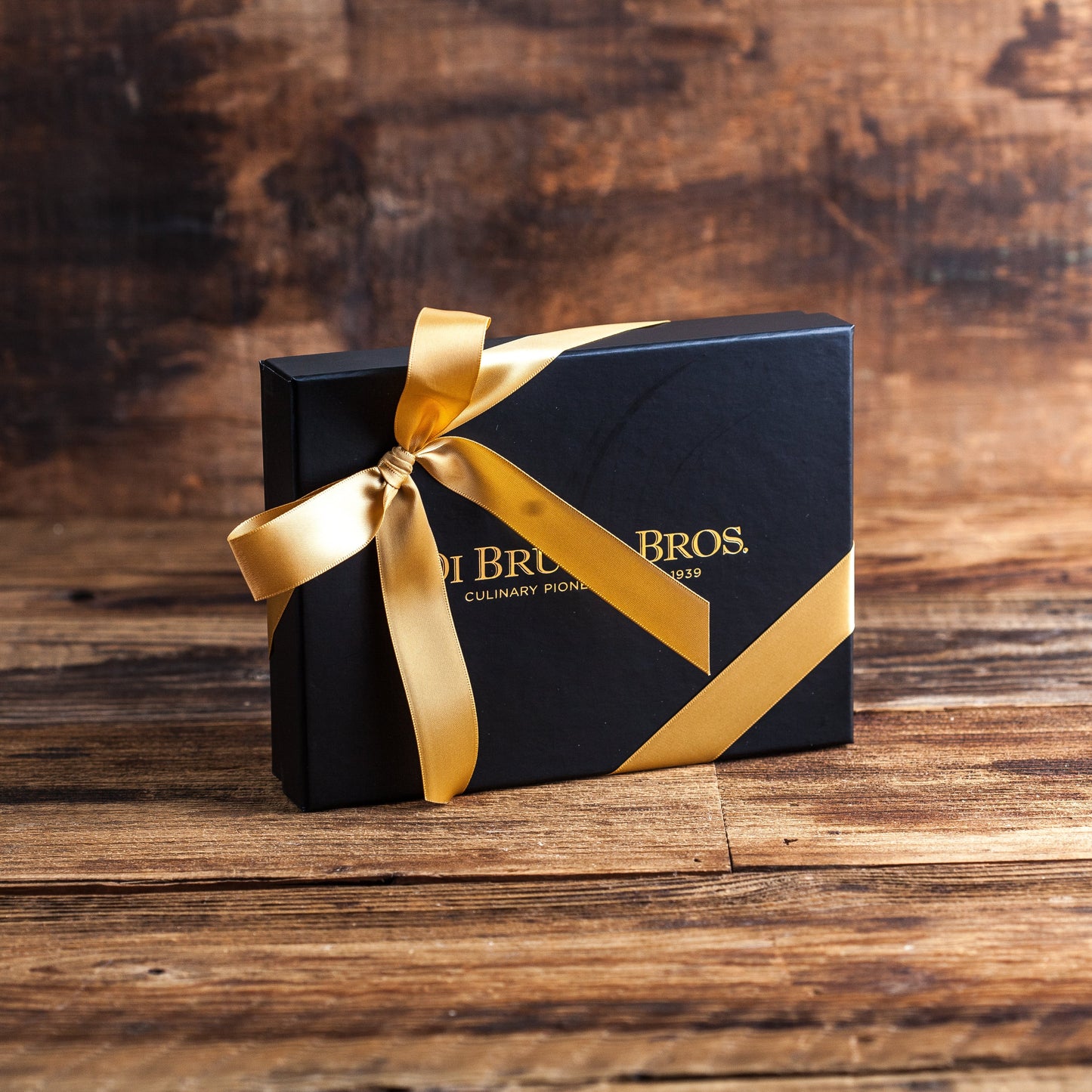 Black gift box with gold ribbon and 'Brisa & Bros' branding on a wooden surface