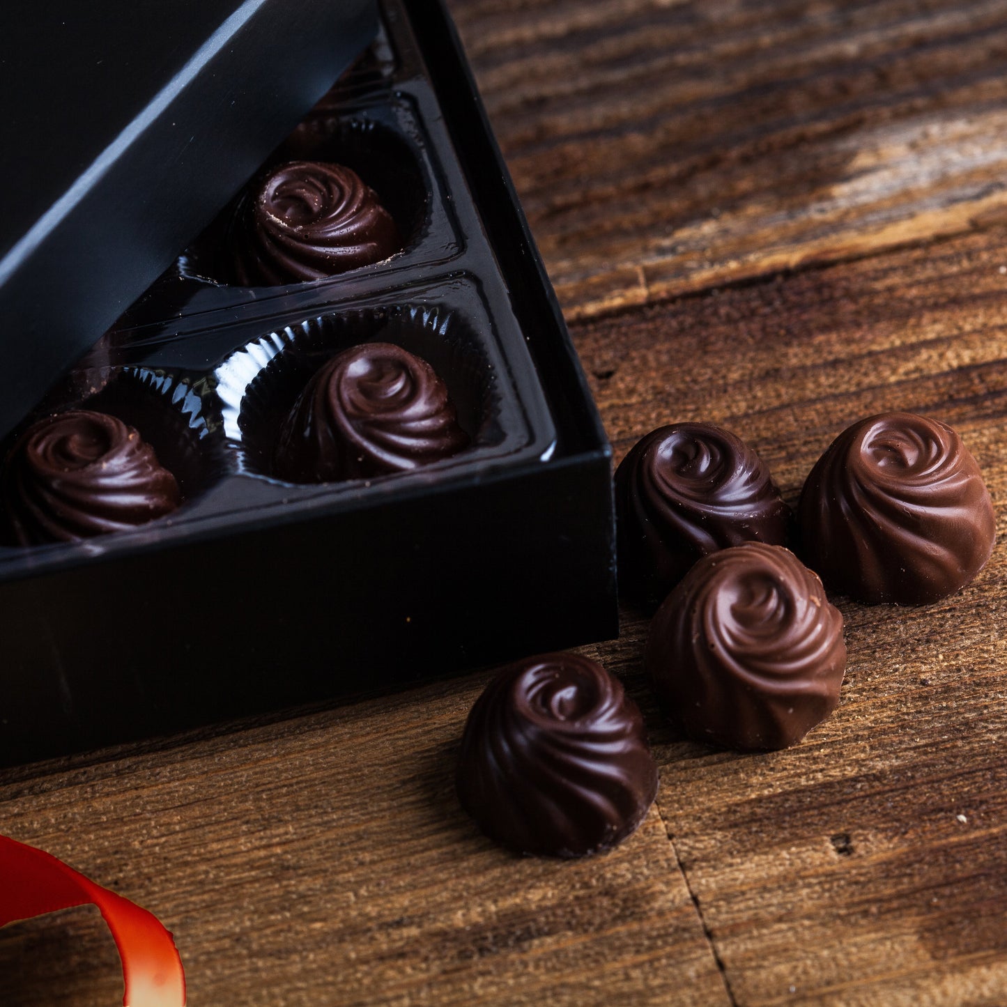 Chocolate truffles in a black box on a wooden surface with a red ribbon.
