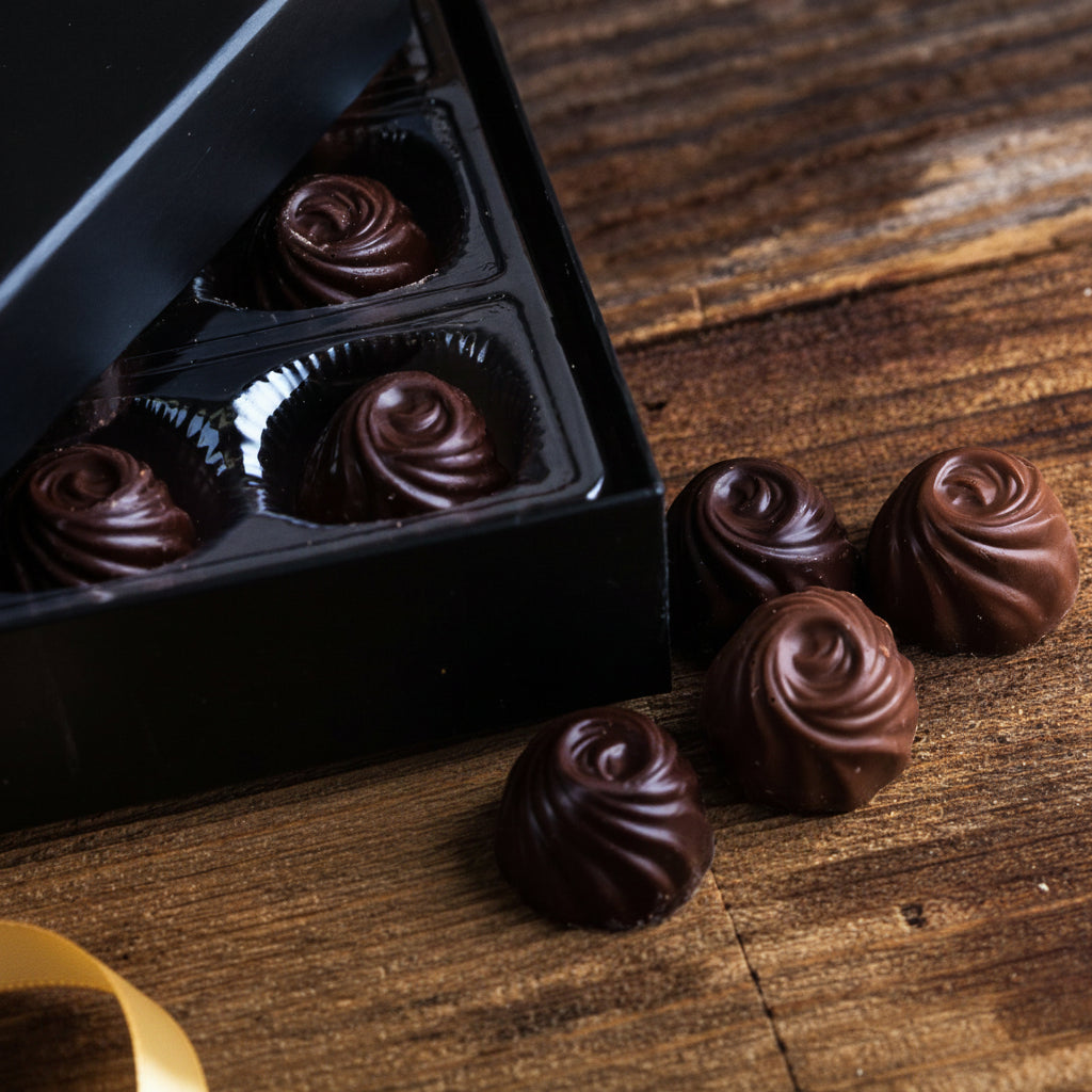 Chocolate truffles in a black box on a wooden surface with a red ribbon.