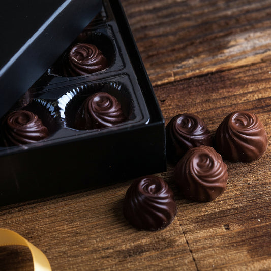 Chocolate truffles in a black box on a wooden surface with a red ribbon.