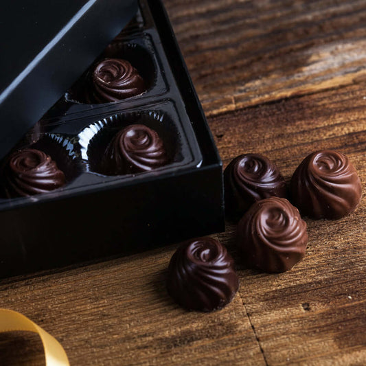 Chocolate truffles in a black box on a wooden surface with a red ribbon.
