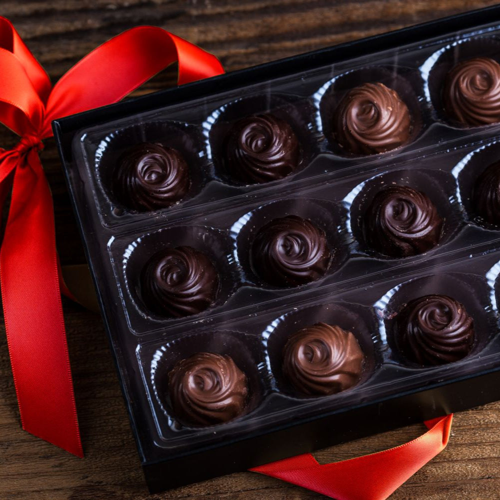 Box of chocolate roses with a red ribbon on a wooden surface