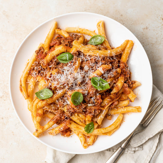 Plate of pasta with tomato sauce, basil leaves, and grated cheese on a light background