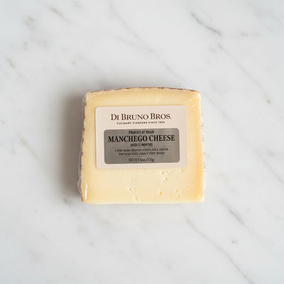 Block of Manchego cheese with Di Bruno Bros label on a dark surface