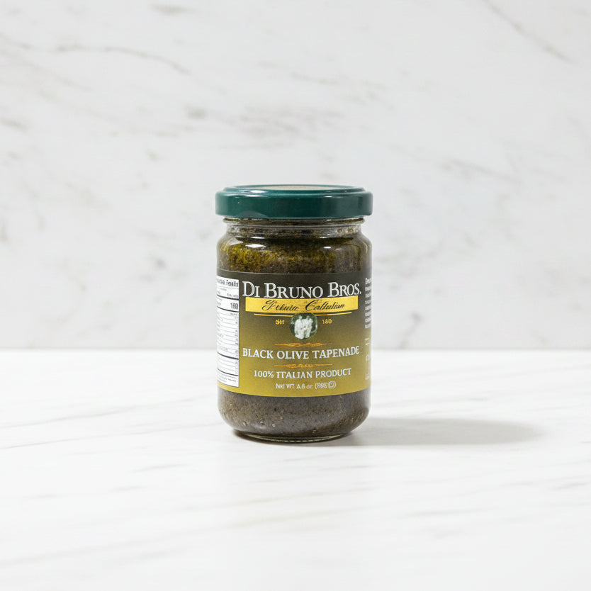 Jar of Di Bruno Bros Black Olive Tapenade on a dark surface with a white textured background
