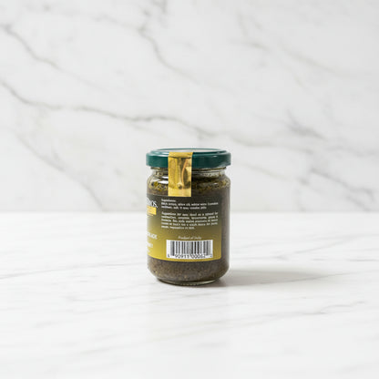 Small glass jar with a green lid on a dark surface with a light-colored wall background