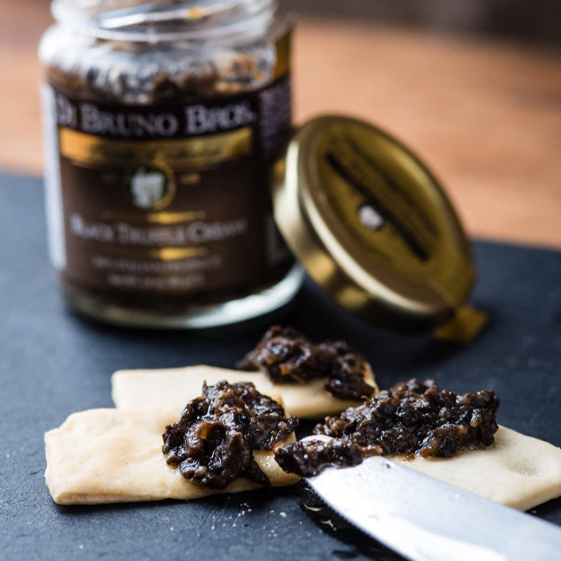 Jar of Di Bruno Bros. Black Truffle Oil with a spreadable food item on a dark surface