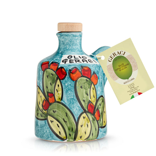 A ceramic bottle of Geraci olive oil with a hand-painted cactus and chili pepper design on a textured turquoise blue background, featuring a light wood cork stopper and a hanging paper tag.