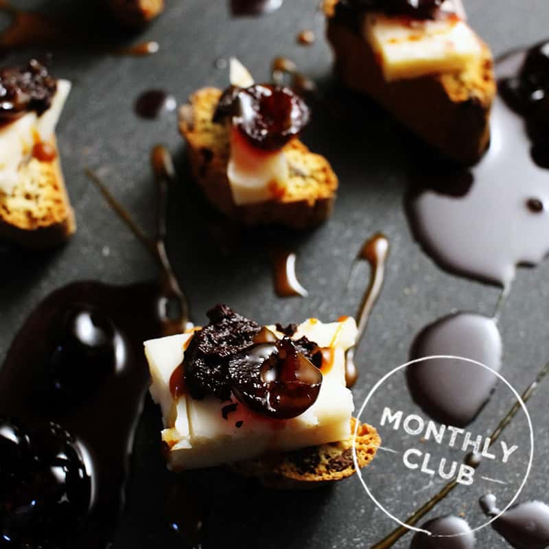 A selection of cheese pairings with crackers, jams, and jellies, drizzled with sauces, on a dark background.