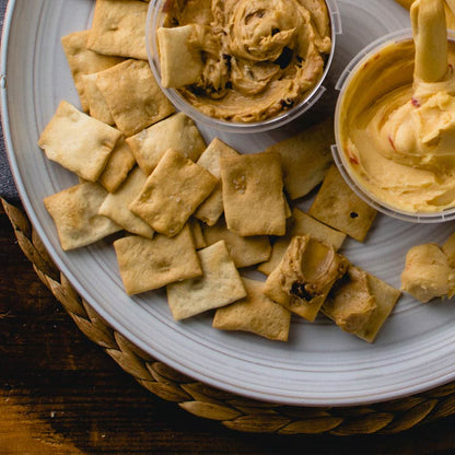 Di Bruno Bros. Crostini Sampler Set is an assortment of flavors including olive oil, parmesan, rosemary, and sea salt, displayed in front of a white background with scattered crostini crackers.