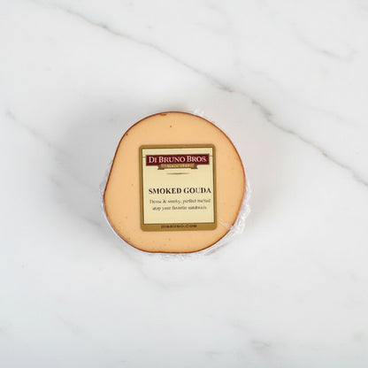 A round piece of smoked gouda cheese with a label in the center displaying the cheese name and brand.