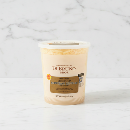 A 12 oz plastic tub of Di Bruno Bros. Shredded Parmigiano Reggiano aged 24 months, featuring a beige label with a brown central panel and a white lid, set against a plain white background.