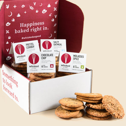 A festive cookie gift box with various labeled packets of cookies including Chocolate Chip and Pretzel Cowboy, alongside some cookies displayed outside the box.