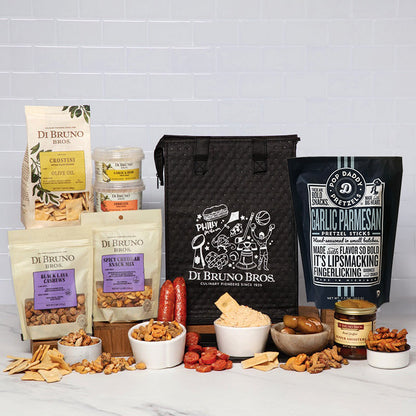 A Di Bruno Bros. gift snack assortment arranged on a white marble surface against a white subway tile wall.
