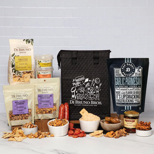 A Di Bruno Bros. gift snack assortment arranged on a white marble surface against a white subway tile wall.