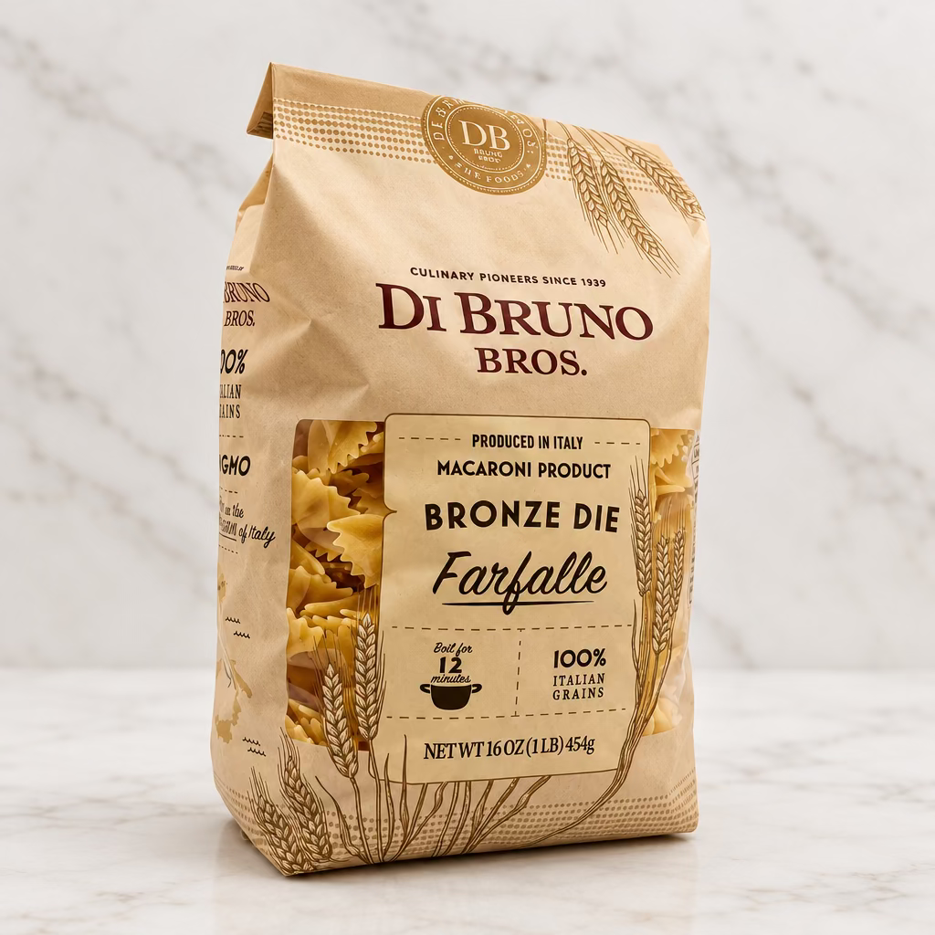 A 16 oz bag of Di Bruno Bros. Bronze Die Farfalle macaroni pasta, featuring a beige paper bag with brown text and wheat illustrations, set against a plain white studio background.